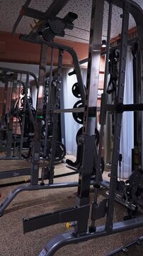 A vertical pan moves upward through a compact hotel gym with a stainless steel Smith rack, cable station, JORDAN weight plates, mirrors, acoustic tiles, curtains, and warm wood.