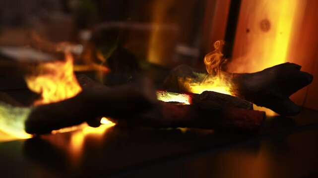 Low angle close up of ceramic logs, embers, and flickering flames, with smoke and glass reflections, warm grading, shallow depth of field, winter interior mood