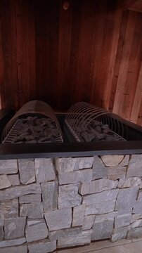Vertical close up shows stacked stone facade, black metal rim, and twin arched steel rock baskets in warm low light, with slow move from wide to tight in an Alpine spa
