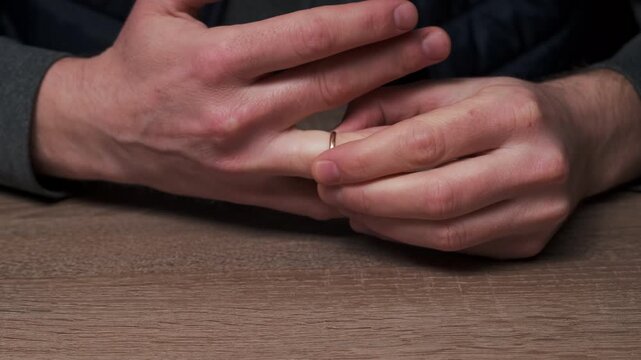 Closeup Hands With Wedding Ring, Man Slowly Removes Ring And Places It On Wood Table, Fingers Fidgeting