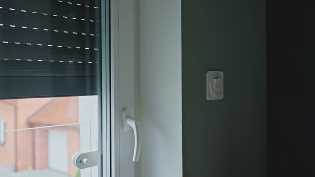 Woman presses wall switch as exterior roller shutter lowers. Concept of home automation, privacy control and residential security
