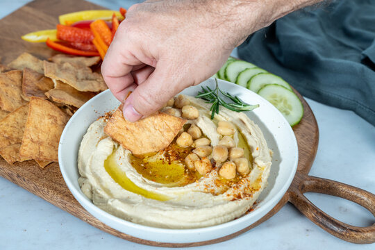 Hummus on a wood cutting board with cucumbers, peppers, pita chips and olive oil 