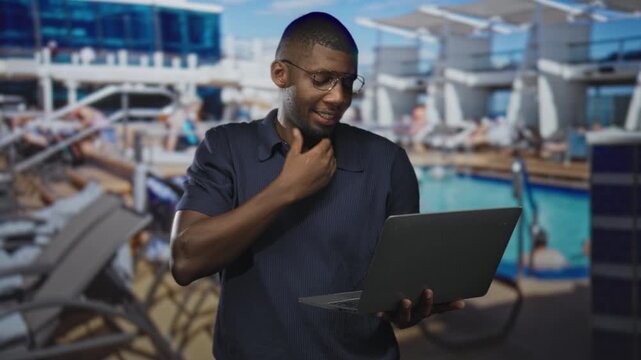Man holding laptop with hand to throat and brief facepalm at poolside inside a building, typing and looking strained; frustration remote work.