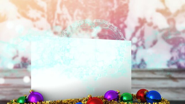 Animation of snow falling over white card with copy space and christmas decoration in winter scenery