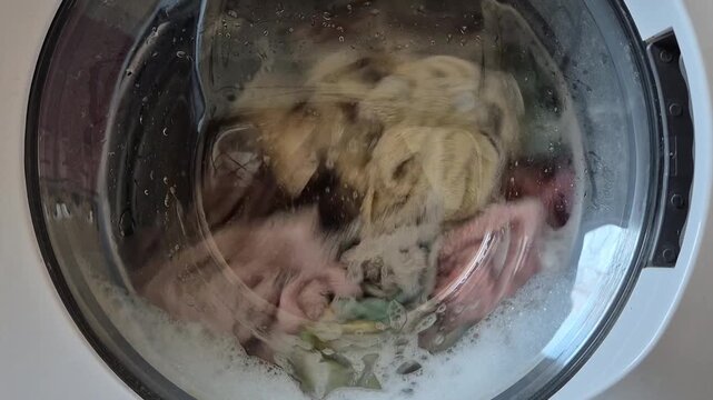Washing machine drum spinning with clothes and water foam close up during laundry cycle