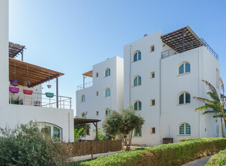 Fototapeta premium Charming white buildings nestled among greenery on a sunny day in a coastal area.