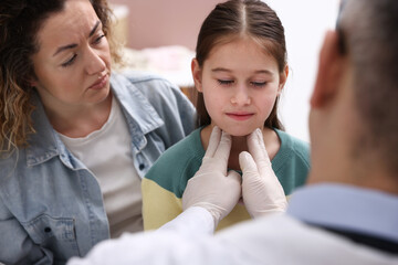 Endocrinologist in medical gloves examining girl's thyroid gland while her smiling mother supporting her indoors, selective focus © New Africa