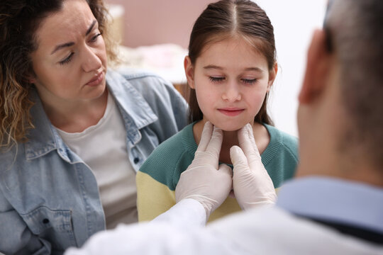 Endocrinologist in medical gloves examining girl's thyroid gland while her smiling mother supporting her indoors, selective focus