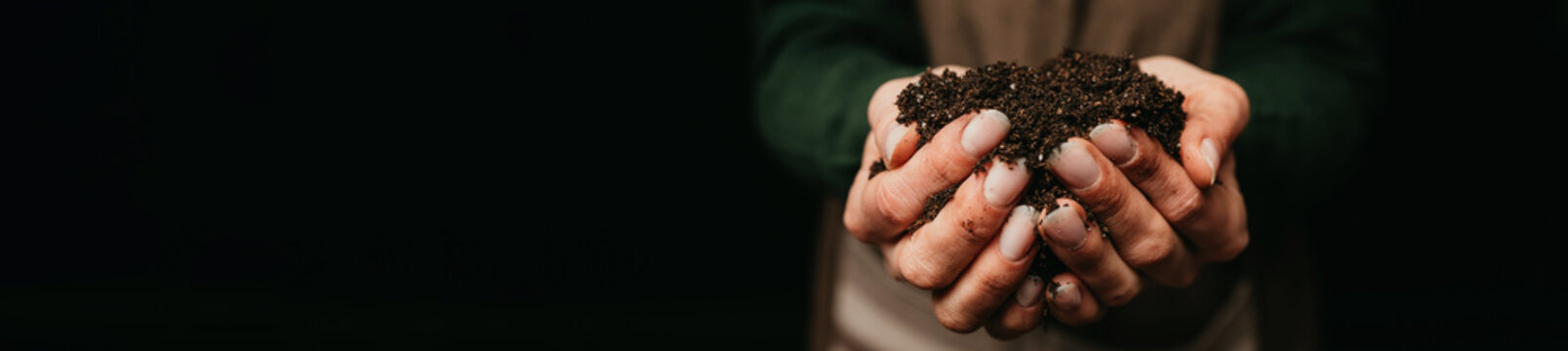 Closeup Hands Holding Rich Soil over dark background.