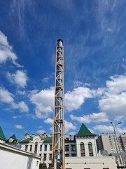 Obraz premium Tall metal chimney pipe rises over city buildings under a blue sky with white clouds