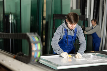Fototapeta premium In workshop for production of glass products, guy co-worker cuts off excess from workpiece and finishes creating plastic panel. .
