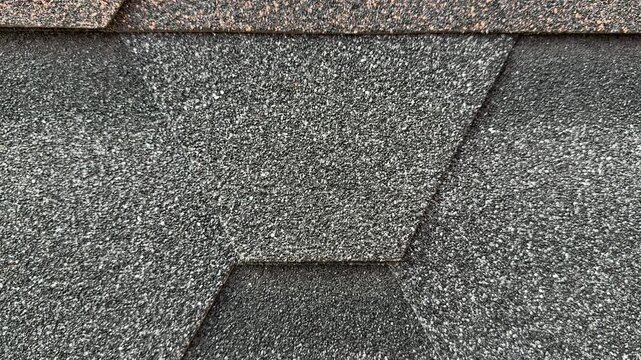 Close-up hexagonal asphalt shingle texture, brown and gray mineral granules, overlapping hexagonal pattern on sloped roof.