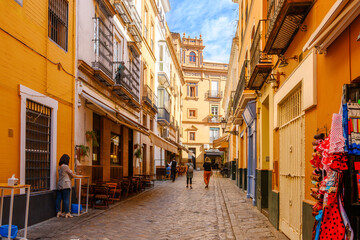 Fototapeta premium A colorful cobblestone side street in the historic Barrio Santa Cruz district, with sidewalk cafes and souvenir shops in the Andalusian city of Seville, Spain.
