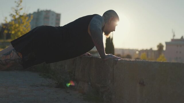 Tattooed muscular man doing push-ups in city park