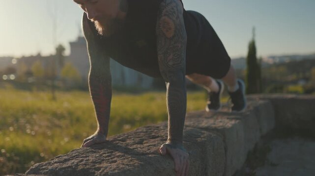 Tattooed athletic man doing push-ups outdoors