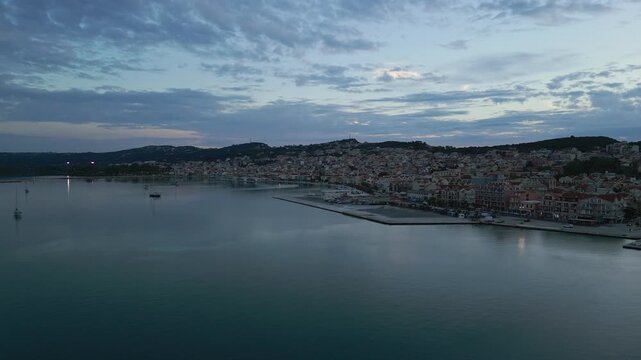 A coastal town at dusk, with boats in the harbor and a hill overlooking the buildings.