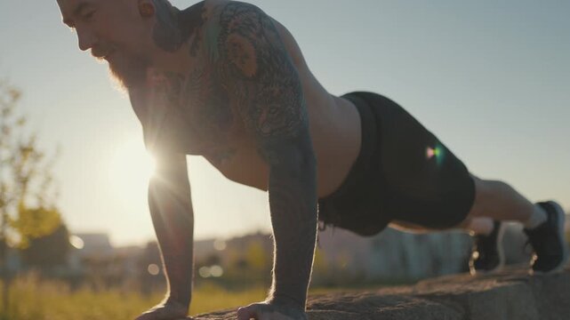 Tattooed muscular man doing push-ups outdoors