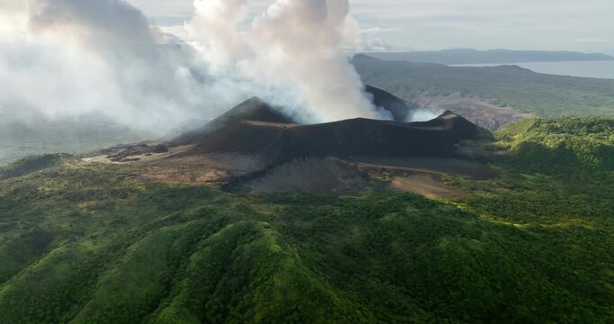 Mount Yasur erupting, sending thick white smoke in cloudy sky above vibrant green jungle and the distant Tanna Island coastline, dramatic volcanic landscape and raw nature. Aerial view drone panorama