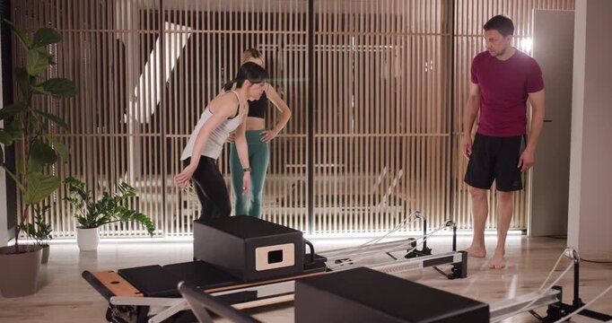Participants engage in a dynamic Pilates session in a stylish studio. An instructor offers support as one member performs advanced movements, focusing on strength and flexibility