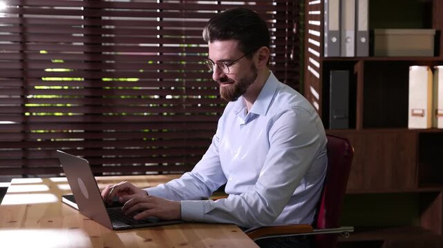Handsome businessman working on laptop at wooden desk in office