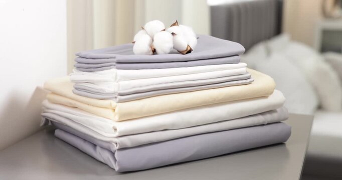 Stack of fresh bed linens and cotton flowers on grey chest of drawers indoors, closeup. Camera moving forward