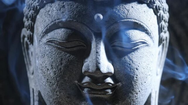 Close up of a stone Buddha face with drifting incense smoke