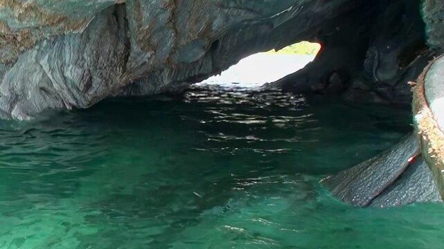Discover the majestic Marble Caves in Patagonia. Serene turquoise water laps against smooth, sculpted marble walls, inviting a gentle boat exploration of this vibrant natural wonder under clear skies.