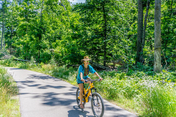 Fototapeta premium Woman rides yellow bike through sunlit forest path