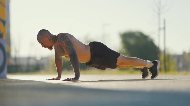 Tattooed muscular man doing push-ups outdoors