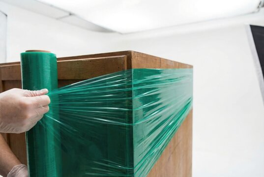 Hands wrapping a wooden furniture cabinet with green protective stretch film