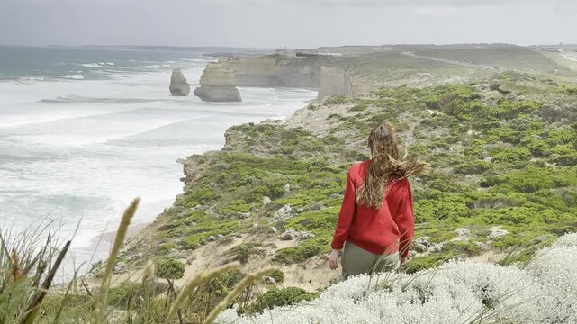 Girl traveler hiking along the Great Ocean Walk admires the view of the Twelve Apostles and the powerful ocean waves on the Great Ocean Road, Victoria, Australia