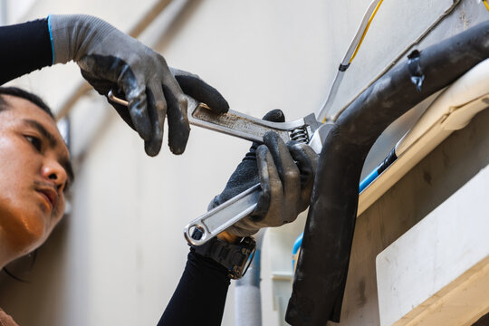 Air conditioning technician hands using adjustable wrenches to tighten copper pipe nut, Professional HVAC contractor installing and repairing outdoor air conditioning unit system
