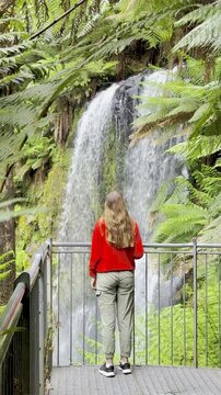 Adventurer girl stands on the viewing platform and admires the powerful Beauchamp Falls in Great Otway National Park, Victoria, Australia, one of the beautiful waterfalls located near Melbourne