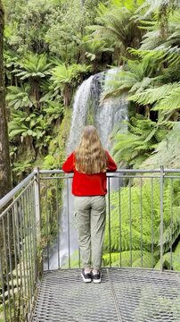 Adventurer girl stands on the viewing platform and admires the powerful Beauchamp Falls in Great Otway National Park, Victoria, Australia, one of the beautiful waterfalls located near Melbourne