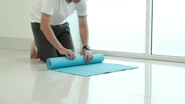 Man rolling out yoga mat at home preparing for fitness workout and wellness routine, highlighting healthy lifestyle, exercise setup, indoor training and minimal space home fitness concept