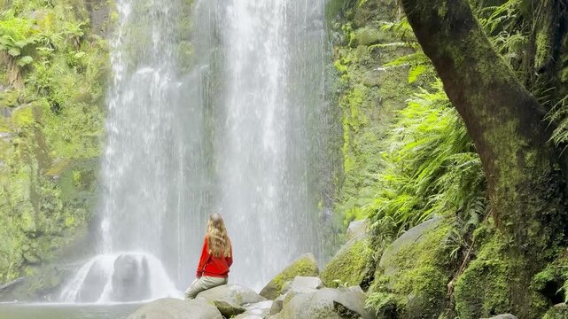 Girl adventurer stands on rock and admires the powerful Beauchamp Falls, surrounded by lush vegetation, located in Great Otway National Park, Victoria, Australia. Stunning waterfalls in the Otways reg