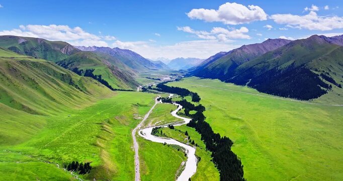 Aerial view of lush green mountain valley with winding river and road under blue sky in Xinjiang, China.