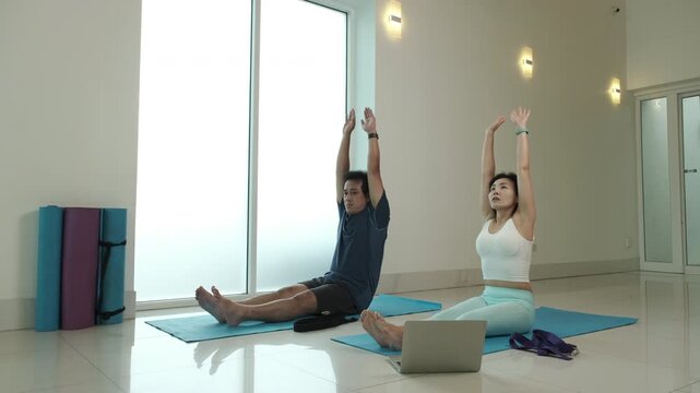 Man and woman practicing seated forward fold yoga pose at home, stretching hamstrings and back, improving flexibility and posture, promoting relaxation and body recovery