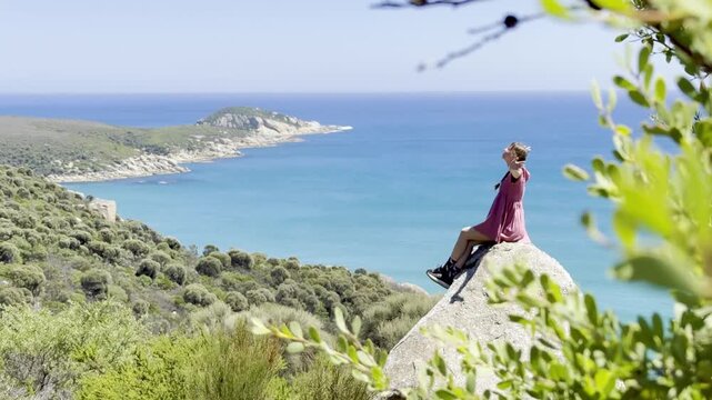 Girl adventurer sits on a large rock with her arms spread, admiring the stunning view over Fairy Cove and the turquoise ocean in Wilsons Promontory National Park, Victoria, Australia