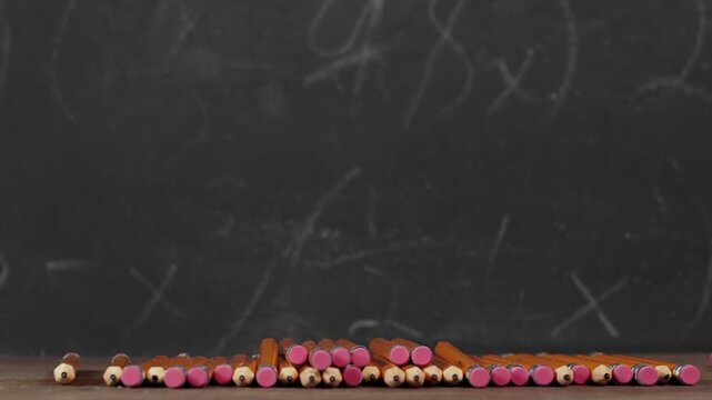 Toy yellow schoolbus driving over school pencils in front of chalkboard. Classic American public school bus traveling quickly over school supplies indicating excitement at going back to school.