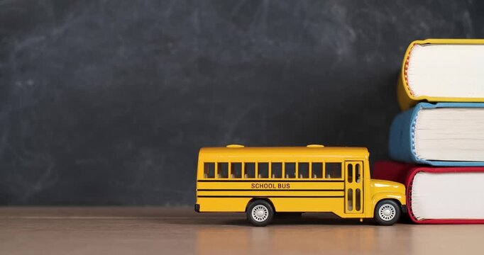 Toy yellow schoolbus driving into school books in front of chalkboard. Classic American public school bus traveling quickly towards school textbooks indicating excitement at going back to school.