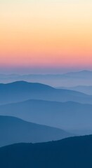 Obraz premium Serene Mountain Layers at Sunrise with Hazy Blue Peaks and Orange Sky.