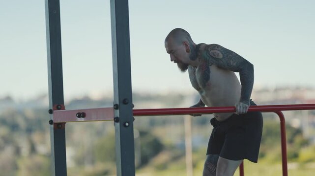 Tattooed muscular man doing triceps dips on parallel bars