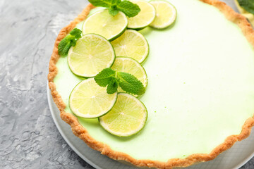 Tasty lime pie with fruit slices and mint leaves on grey textured table, closeup © New Africa
