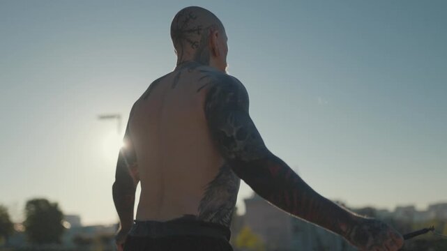 Tattooed muscular man skipping rope outdoors during sunset workout