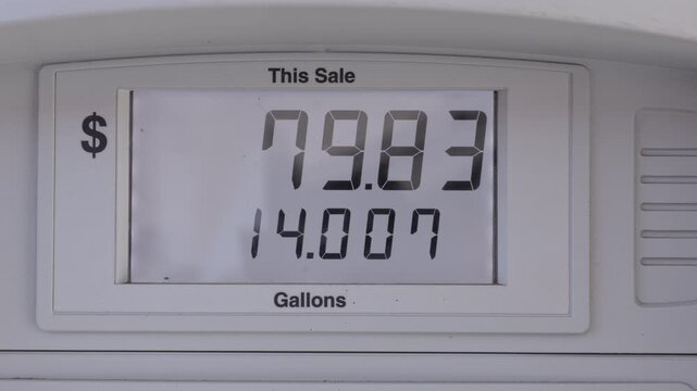 Gas pump display shows high totals and gallon counts, closeup digital meter indicating sale amounts and gallons, white bezel and clear digits, visible watermark, retail station context