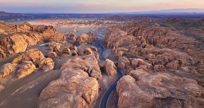 Aerial view of a winding asphalt road through desert Yardang formations during sunset in Xinjiang, China.