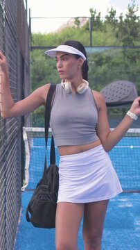 Vertical video: Camera approaching, leaning woman posing with racket on blue court, wearing visor