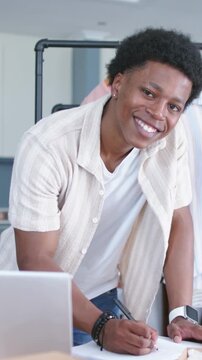 Vertical video: Leaning forward man in striped top noting designs at studio, with laptop and pen