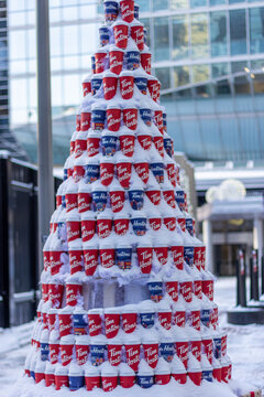 Canada, Montreal, 24 December 2025 : Snowy coffee cup tree sculpture outside glass building winter scene